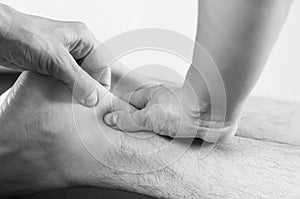 Closeup of hands of chiropractor/physiotherapist doing calf muscle massage to man patient in white and black.