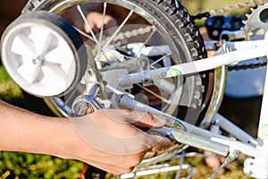 Closeup on hands of father fixing mechanism of the bicycle, green background outside