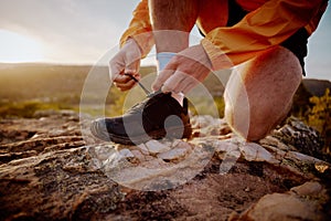 Closeup of hands of fit male jogger tying shoelaces preparing for cross country mountain trail run in nature during