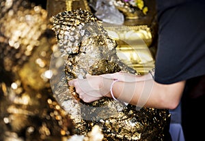 Closeup of hands gilding gold leaf sheet to Buddha statue in Thai temple