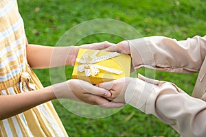Closeup hands giving gift box,Asian daughter and mother with gift box in green nature background,parent giving her birthday little