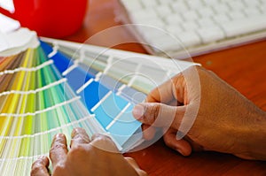 Closeup hands holding palette, colormap spread out in front of white computer keyboard, designer concept