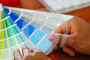 Closeup hands holding palette, colormap spread out in front of white computer keyboard, designer concept