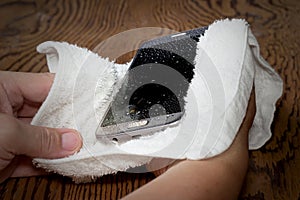 Closeup Hands holding White cloth with wet smart phone drops on wooden floor