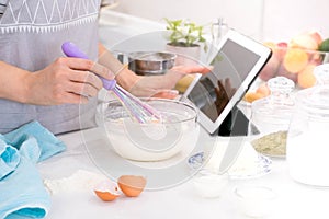 Closeup hands lady standing in kitchen and cooking the dough. Looking at tablet computer. Female following recipe on