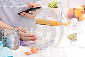Closeup hands lady standing in kitchen and cooking the dough. Looking at tablet computer. Female following recipe on