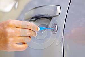 Closeup hands of locksmith using pick tools to open locked car door