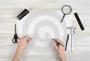 Closeup hands of man holding pencil and drawing on white paper in top view. Draftsman workplace equipped with ruler, pen