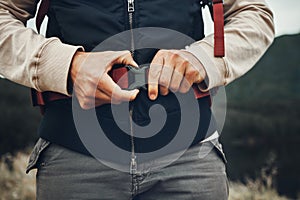 Closeup hands, man and nature fastening a backpack for hiking, trekking or travel in the mountains. Walking, buckle clip