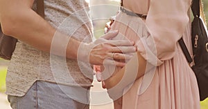 Closeup hands of man touching pregnant belly of his woman in park.