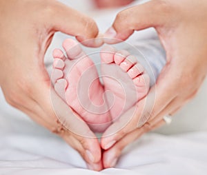 Closeup of hands of a parent forming a heart shape around tiny newborn baby feet. Mother loving her little baby. Small