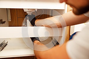 Closeup of hands of professional plumber fixing sink, changing water pipe in apartment