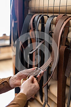 Closeup hands of professional tanner choosing belt buckle on wooden table at leather workshop