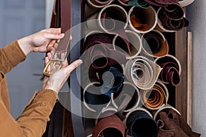 Closeup hands of professional tanner choosing belt buckle on wooden table at leather workshop