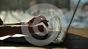 Closeup hands of unrecognizable female freelancer typing on laptop sitting at desk on background of window and bright