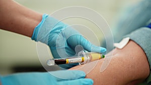 Closeup hands of unrecognizable female nurse in gloves drawing sample of blood from vein on male patient arm for testing