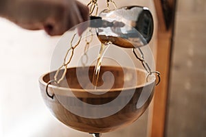 Closeup hands of unrecognizable specialist pouring hot aromatic oil into bowl during preparation for exotic Shirodhara