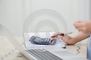 Closeup hands of woman calculating finance household with calculator on desk at home.