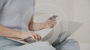 Closeup hands of woman sitting on bed using laptop computer shopping online with credit card buying.