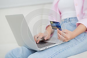 Closeup hands of woman sitting on sofa using laptop computer online shopping with credit card.