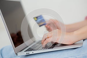 Closeup hands of woman sitting on sofa using laptop computer online shopping with credit card.