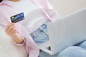 Closeup hands of woman sitting on sofa using laptop computer online shopping with credit card.