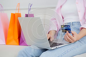 Closeup hands of woman sitting on sofa using laptop computer shopping online with credit card while paper bag.