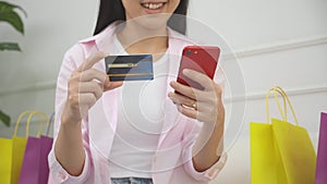 Closeup hands of woman sitting on sofa using smart phone shopping online with credit card buying to internet.