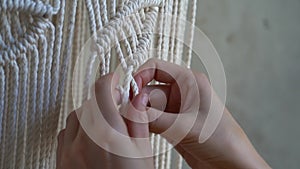 Closeup hands of woman working on half-finished macrame piece, weaves lamp shade for chandelier