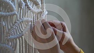 Closeup hands of woman working on half-finished macrame piece, weaves lamp shade for chandelier