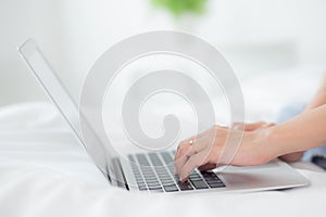 Closeup hands young asian woman sitting on bed using laptop computer working from home in the bedroom.