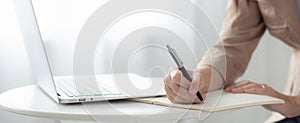 Closeup hands young asian woman writing on notebook for planning working and using laptop computer on desk.