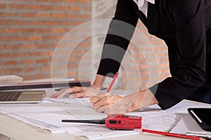 Closeup hands young caucasian architect woman looking laptop and working drawing blueprint for planning building house.