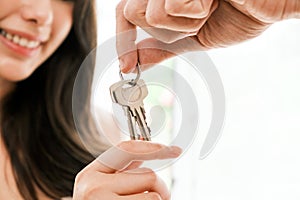 Closeup hands of young happy Asian couple showing, holding keys to the camera inside their new home. Moving, relocating.