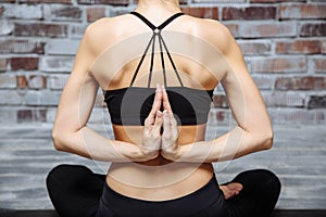 Closeup hands of young woman practicing yoga with namaste behind the back, sitting in seiza exercise, vajrasana pose, home interio