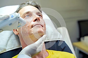 Closeup handsome man having color light therapy to stimulate facial skin by professional cosmetologist wellbeing