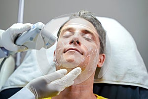 Closeup handsome man having color light therapy to stimulate facial skin by professional cosmetologist wellbeing