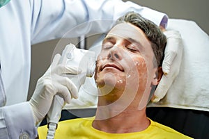 Closeup handsome man having color light therapy to stimulate facial skin by professional cosmetologist wellbeing