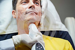 Closeup handsome man having color light therapy to stimulate facial skin wellbeing