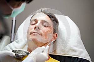 Closeup handsome man receiving skin gel to prepare the color light therapy to stimulate facial health