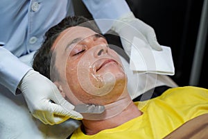 Closeup handsome man receiving skin gel to prepare the color light therapy to stimulate facial health