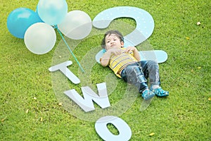 Closeup happy asian kid lie on grass floor in park textured background in 2 nd years anniversary concept