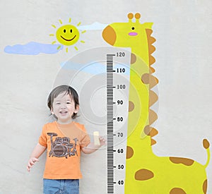 Closeup happy asian kid stand for measure height with cute cartoon at the marble stone wall textured background