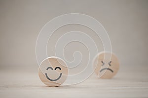 Closeup happy emotion face on wooden piece with unhappy one behind for satisfaction survey