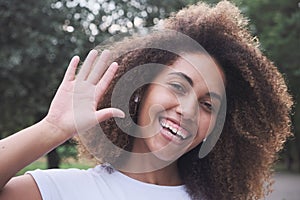 Closeup happy face biracial modern female in wireless earphones smiling waving hand outdoor
