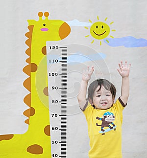 Closeup happy asian kid stand for measure height with cute cartoon at the marble stone wall textured background in growth of kid c