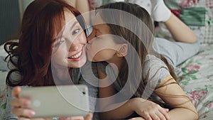 Closeup of happy mother and little girl taking selfie photo with smartphone camera and have fun grimacing while sitting