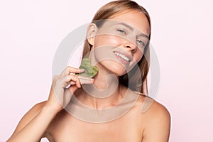 Closeup of happy smiling beautiful half naked girl doing face skin massage and looking at camera isolated over white