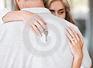 Closeup of happy wife hugging husband while holding keys after buying first home. Couple relocating to new house or