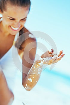 Closeup on happy woman in swimsuit sitting on beach and pl